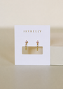 The JaxKelly Open Mini Hoop Earrings in Pink feature gold plating and pink stone accents, are hypoallergenic for sensitive ears, and come displayed on a white JaxKelly card against a neutral background.
