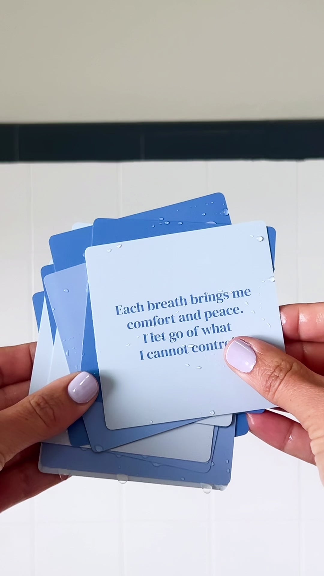JaxKelly's Calm Shower Affirmations, slightly wet, being displayed and shuffled through by a pair of hands.