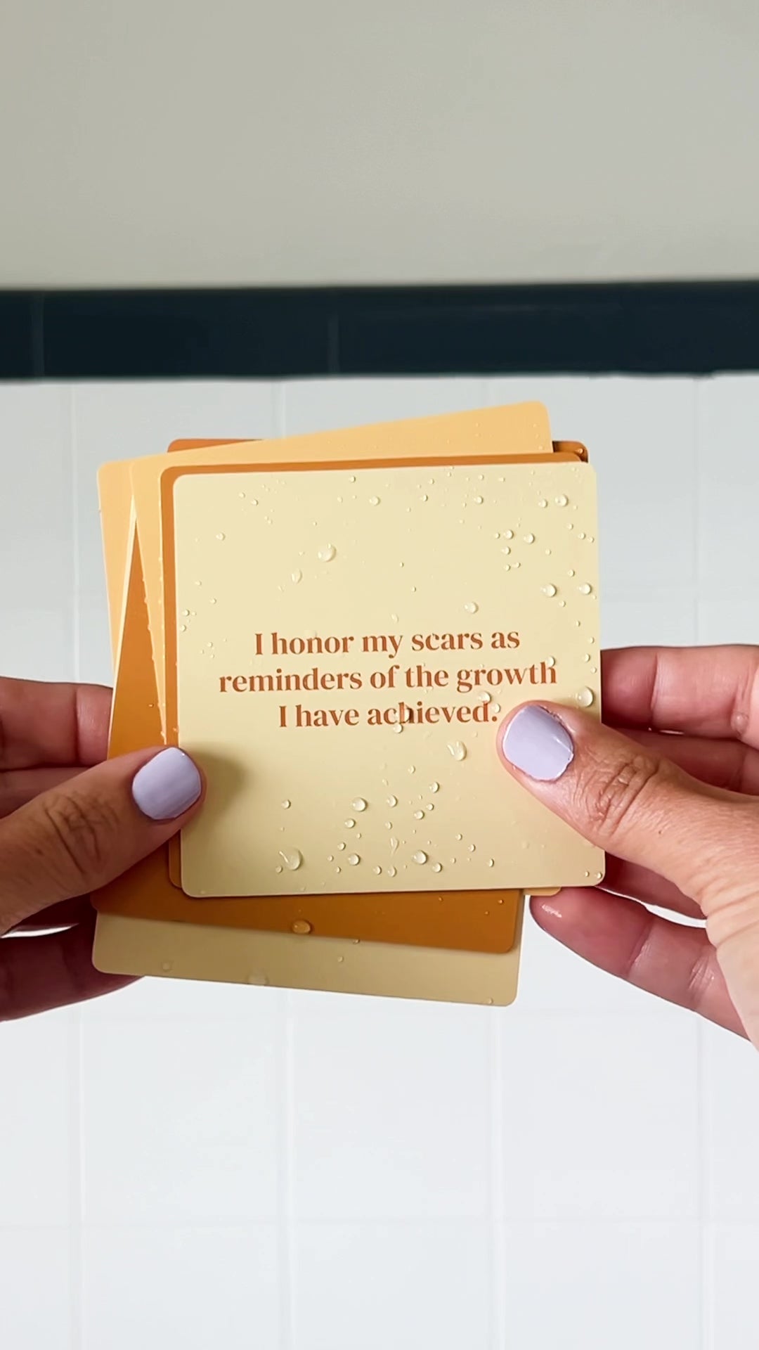 JaxKelly's Strength Shower Affirmations, slightly wet, being displayed and shuffled through by a pair of hands.