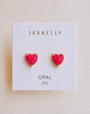 The JaxKelly Puffed Heart - Pink Opal stud earrings feature lab-grown pink opal and 18k gold plating, displayed on a white card that reads “JAXKELLY OPAL joy.”.