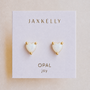 Elegant and hypoallergenic, the JaxKelly Puffed Heart - White Opal earrings feature heart-shaped opals with gold-plated studs, displayed on a white card labeled with “JaxKelly,” “Opal,” and “joy” in gold lettering—perfect for any occasion.