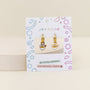 A pair of Ramen Enamel Charm Hoop kids earrings displayed on a JaxKelly card with colorful geometric designs labeled “hypoallergenic” and “kid-friendly posts.” Perfect for sensitive ears, these hoops feature fun ramen charms.