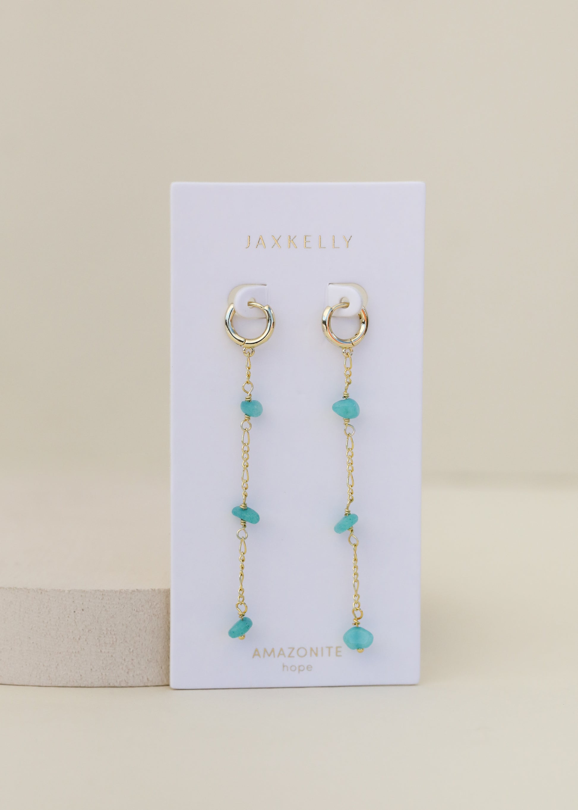 A pair of Raw Gemstone Chain Drop Earrings in tarnish-free gold featuring dangling chains and turquoise Amazonite stones, displayed on a white JaxKelly card labeled “AMAZONITE hope” against a neutral background.