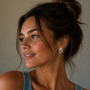 A woman with brown hair in a messy bun, wearing a sleeveless denim top and JaxKelly's Silver Bold Wave statement stud earrings, smiles softly as she looks to the side against a neutral background.