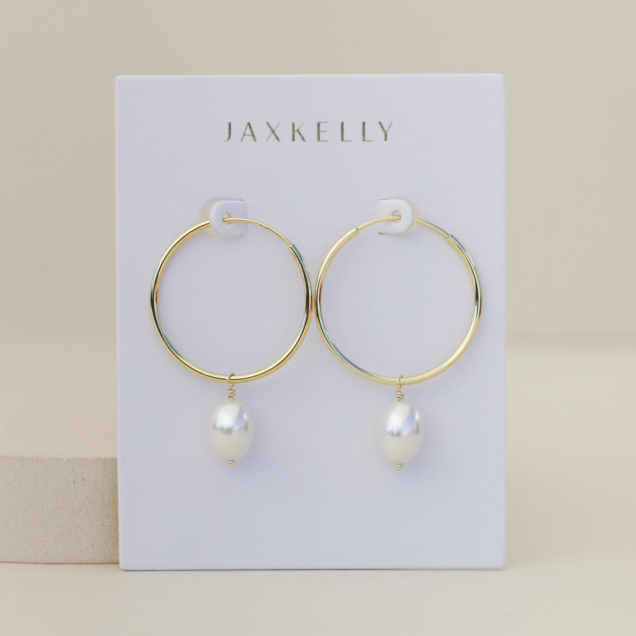 The Simple Hoop with Pearl features minimalist gold hoops with white pearls, presented on a white JaxKelly card against a neutral backdrop.