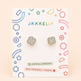 A pair of Snowflake Enamel Flat Back Kids Earrings by JaxKelly rests on a colorful display card labeled Hypoallergenic and Kid-Friendly Posts, with playful geometric patterns decorating the card’s border.