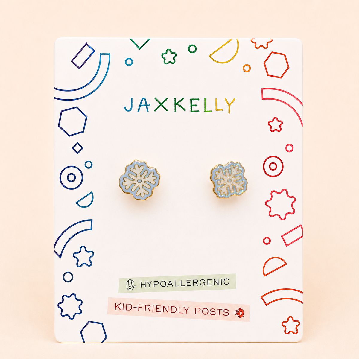 A pair of Snowflake Enamel Flat Back Kids Earrings by JaxKelly rests on a colorful display card labeled Hypoallergenic and Kid-Friendly Posts, with playful geometric patterns decorating the card’s border.