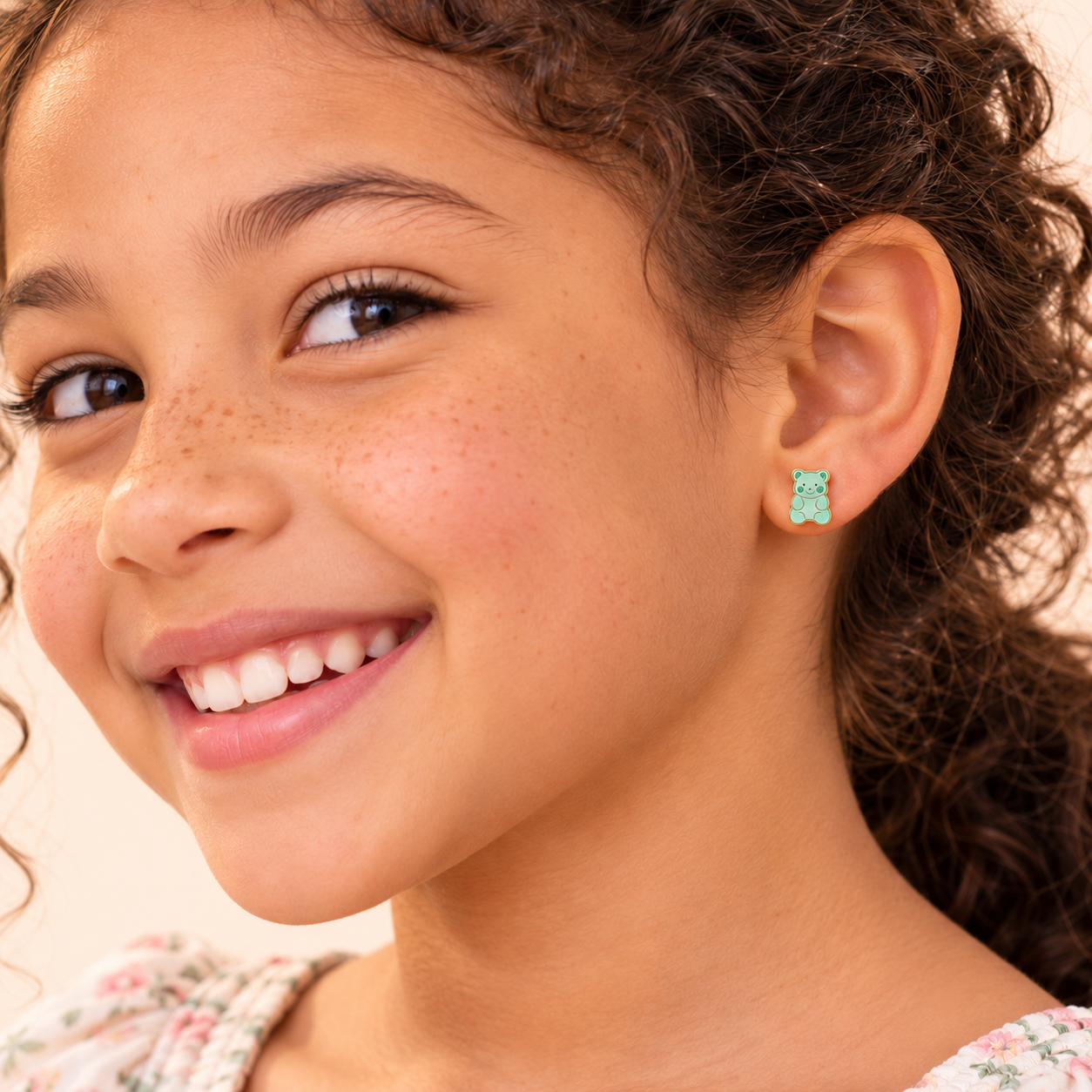 A smiling child wearing a light green, gummy bear-shaped Sugar Bear Flat Back Kids Earrings hypoallergenic earring.