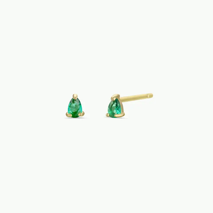 A pair of JaxKelly Teardrop Stud - Emerald CZ earrings is displayed on a plain white background. One earring faces forward to showcase the green pear-shaped CZ gemstone, while the other is positioned flat to reveal the 18k gold plated post.