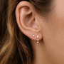 Close-up of a woman's ear with two piercings, wearing JaxKelly’s Mini Baguette Drop - White CZ: a simple gold stud and an elegant drop earring with a rectangular and hanging gem—tarnish-free jewelry for any occasion.