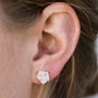 Close-up of a person’s ear wearing the White Druzy Prong, a geometric hexagon stud earring with a natural white druzy stone and gold prongs, set in 18k gold plated sterling silver. Complements light skin and light brown hair.