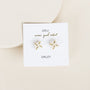 A pair of 18k gold plated, X-shaped White Druzy Prong stud earrings displayed on a white JaxKelly card with "wear good vibes" and "DRUZY" printed below, set against a neutral light background.