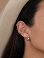 Close-up of a woman’s ear wearing the Bold Hoop, along with a wavy stud and sterling silver ear cuffs. Part of her dark hair and a beige hat can also be seen.