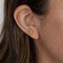 Close-up of a woman's ear with straight brown hair wearing the Offset Trio - White CZ, a small 18k gold plated stud earring shaped like three stacked leaves, each adorned with white cubic zirconia, against a softly blurred background.