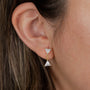Close-up of a person’s ear wearing the Dual Triangle Drop earring, featuring gold plating, two connected clear triangle-shaped CZ stones, and secure sterling silver posts. The design dangles slightly below the earlobe.