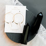 The Clear Quartz Hoop - Healing earrings are showcased on a JaxKelly healing stone card, beside two large black crystals on a dark round surface—a stunning piece of handcrafted jewelry.