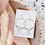 The Amazonite Hoop - Hope earrings feature gold-plated hoops with light green amazonite stone pendants, displayed on a card against pink cloth, pampas grass, and a terrazzo-patterned backdrop.