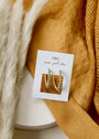 The Large Ball Hoop features gold-plated hoops with sterling silver posts, displayed on a white JaxKelly card that reads "wear good vibes," set atop a soft surface with beige pampas grass and mustard yellow textured fabric.