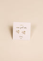 A pair of delicate gold and pearl White Opal Crown Stud earrings rest on a white JaxKelly card reading "wear good vibes" and "lab-grown opal joy," set against a neutral beige background.