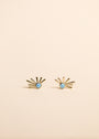 The Sun Ray - Fire Opal stud earrings feature lab-grown Fire Opal gems at the center, each with six gold rays and 18k gold plating, shown on a plain beige background.