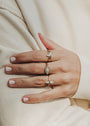 A close-up of a hand with light pink nail polish, wearing the Amazonite Point Ring and two gold gemstone rings, rests on cream fabric, highlighting chic minimalist jewelry.