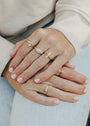 Close-up of hands with light pink nails wearing the Amazonite Point Ring and other gold rings with opal and white stones—an ideal minimalist jewelry look—resting on light blue jeans and a cream long sleeve top.