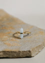 The Amazonite Point Ring features a vertical, pale blue Amazonite stone set in gold. This minimalist piece is displayed centered on a textured, light brown stone surface with a simple background.