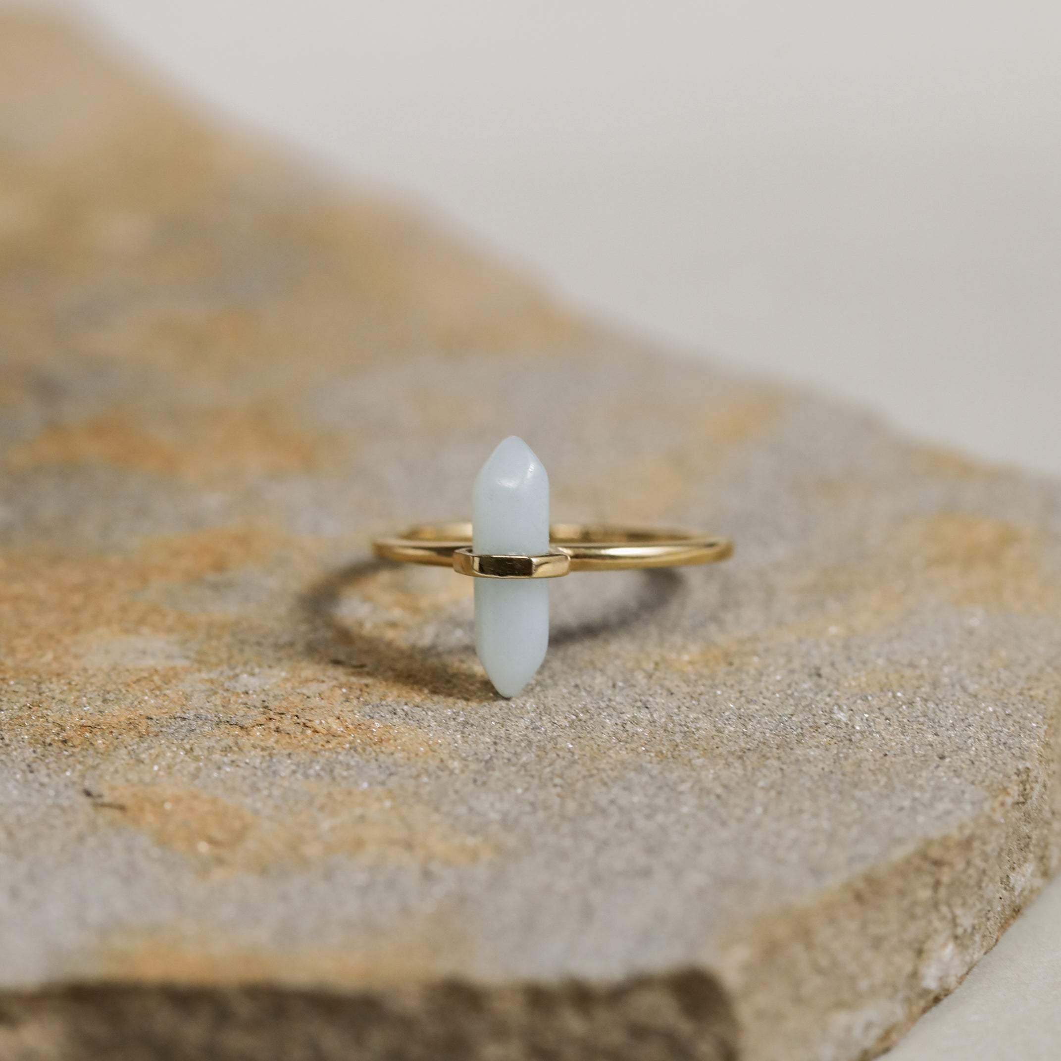 The Amazonite Point Ring is a minimalist gold ring featuring a light blue, pointed Amazonite stone set vertically atop a textured band.