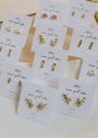 A set of ten pairs of “Sun Ray - Fire Opal” stud earrings, each on a white “JaxKelly” card, featuring 18k gold plating, sun ray shapes, and lab-grown fire opal stones with colorful accents.