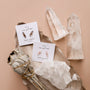 A flat lay features a Smoky Quartz Mineral Point for protection, crystals, sage, and two pairs of polished gemstone earrings—one 18k gold plated, one sterling silver—on cards labeled Smoky Quartz and Rose Quartz atop a beige background with a metallic leaf dish.