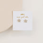 The Pavé Flower features 18k gold plated, flower-shaped stud earrings with small clear stones and sterling silver posts, displayed on a white card that reads JEWELRY more good vibes on a light, neutral background.