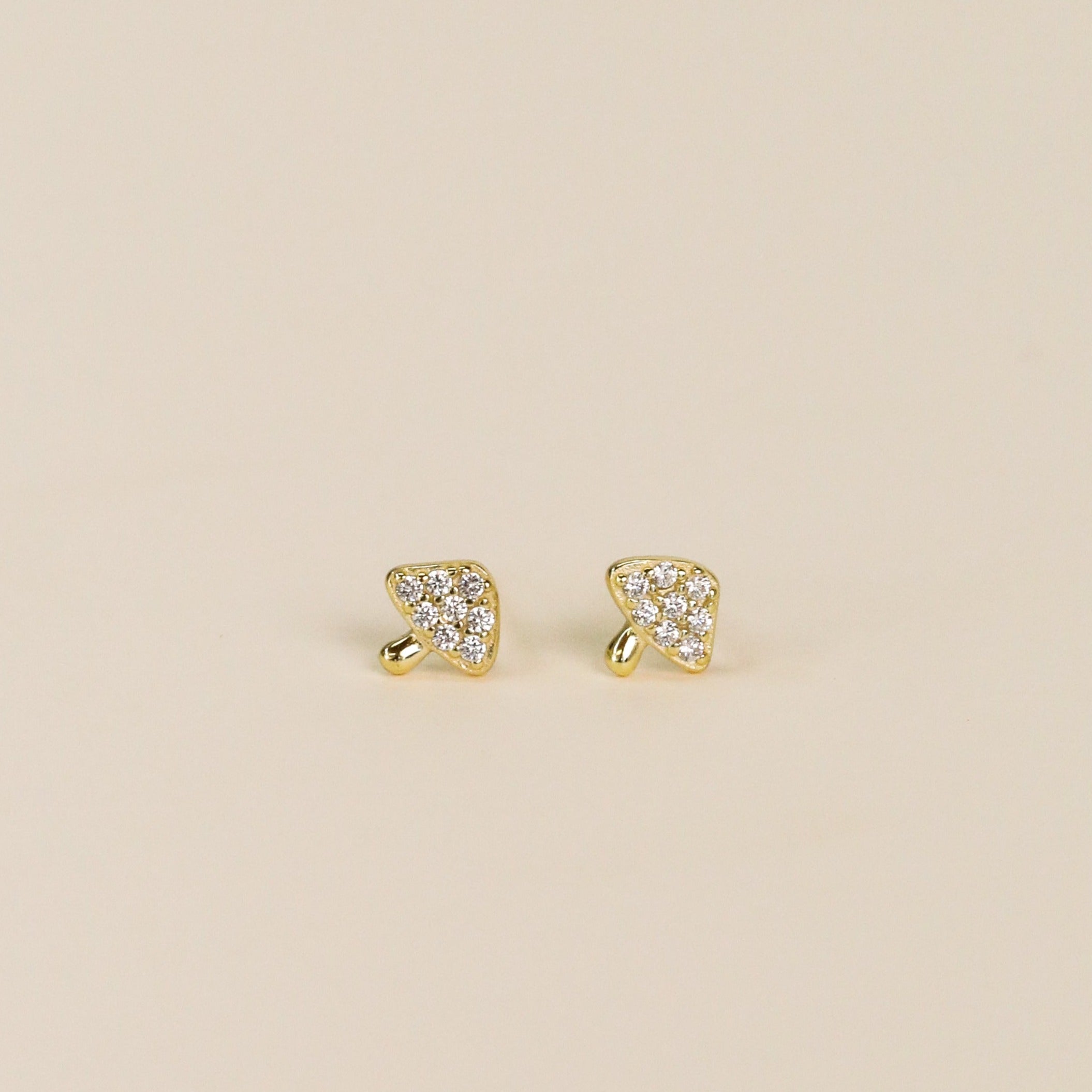 A pair of Pavé Mushroom small, gold-plated triangular stud earrings with a textured finish and sparkling CZ accents, displayed on a plain light beige background.