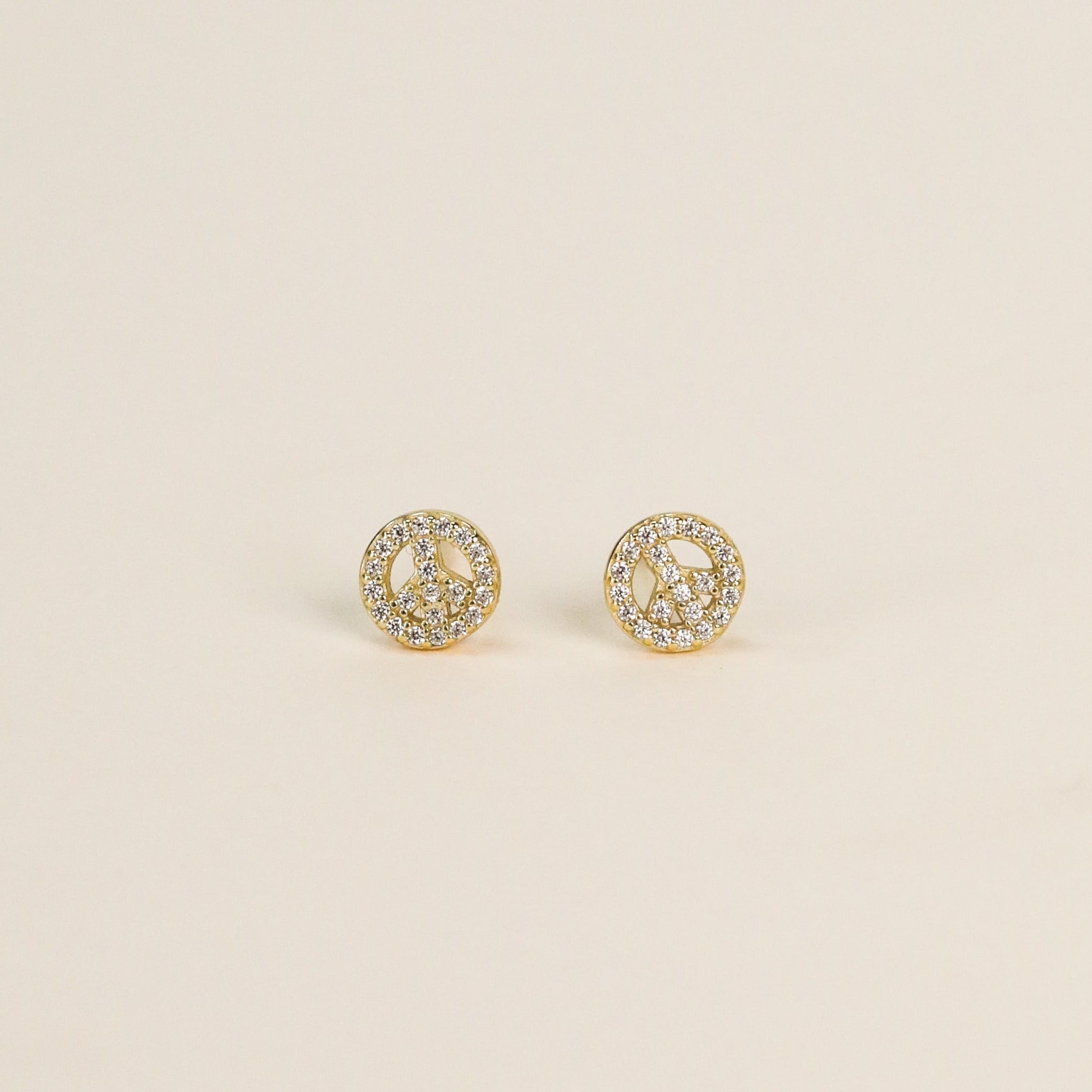 A pair of small, round 18k gold plated Pavé Peace Sign stud earrings with clear CZ stones, displayed on a plain light background.