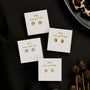Four pairs of Pavé Mushroom gold plated earrings are displayed on white cards labeled “wear good vibes,” arranged on a black fabric background with dried plants and part of an animal print plate visible.