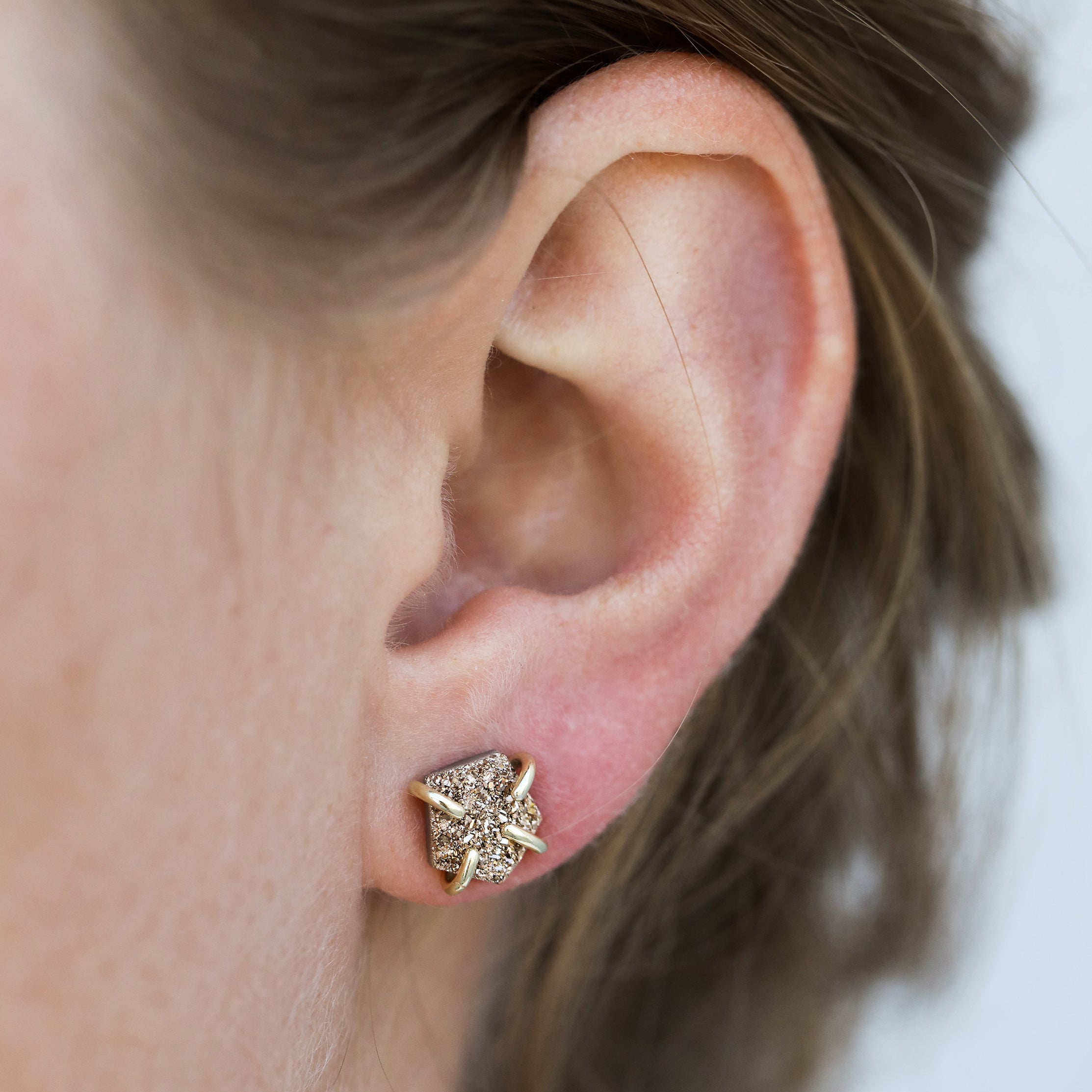 Close-up of a person’s ear wearing the Rose Gold Druzy Prong earring, featuring a star shape with sparkling gemstones and elegant 18k gold plating. The person's brown hair is pulled back against a softly blurred background.