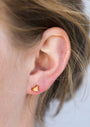 Close-up of a person's ear wearing the Citrine - Mini Energy Gems - Success stud earring, featuring a small gold triangle design with 18k gold plating and sterling silver posts; light brown hair strands frame the background.