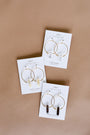 The Clear Quartz Hoop - Healing earrings are displayed on a labeled white card against a light brown background, featuring handcrafted gold hoops with clear quartz crystal charms—perfect for fans of artisan jewelry.