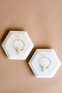 JaxKelly’s Citrine Hoop - Success earrings, featuring gold hoops and clear crystal pendants, are displayed on white hexagonal marble trays—a stylish, hypoallergenic choice for elegant wearers.