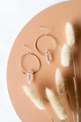 Clear Quartz Hoop - Healing earrings are displayed on a peach surface beside dried beige bunny tail grass, creating a minimal, elegant backdrop that highlights the beauty of this handcrafted jewelry.
