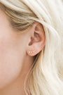 Close-up of a woman's ear with light blonde hair, wearing the White Crawler—an 18k gold-plated ear climber adorned with small cubic zirconia arranged in a curved line along the earlobe.