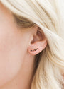 Close-up of a person's ear with light blonde hair, wearing the Black Crawler—a delicate curved Sterling Silver earring set with small black stones and a protective coating. The softly blurred background highlights its elegant detail.