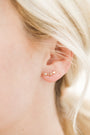 Close-up of a person with blonde hair wearing the Star & Constellation 18k gold plated earring, featuring a row of small stars for celestial charm. The softly blurred background highlights the elegant design.