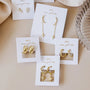 Five pairs of Pavé Gold Hoop 18k gold plated earrings, including square and CZ styles, are displayed on white JAYCELLY wear good vibes cards on a beige surface next to a glass dish.