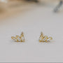 The Offset Trio - White CZ features delicate stud earrings with three baguette-cut white CZ stones in a fan shape, finished in 18k gold plating and presented on a neutral surface.
