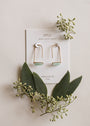 The Amazonite Gemstone Drop - Hope earrings, elegantly 18k gold plated, are displayed on a white JaxKelly card among green leaves and small sprigs on a light background.