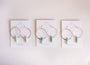 Three pairs of gold plated Amazonite Hoop - Hope earrings with light blue stone pendants are displayed on white JaxKelly Wear Good Vibes cards, arranged side by side on a light background.