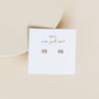 The Lilac Baguette rectangular stud earrings with 18k gold plating are shown on a white card labeled “JAXKELLY wear good vibes” in gold and black, set against a beige background.