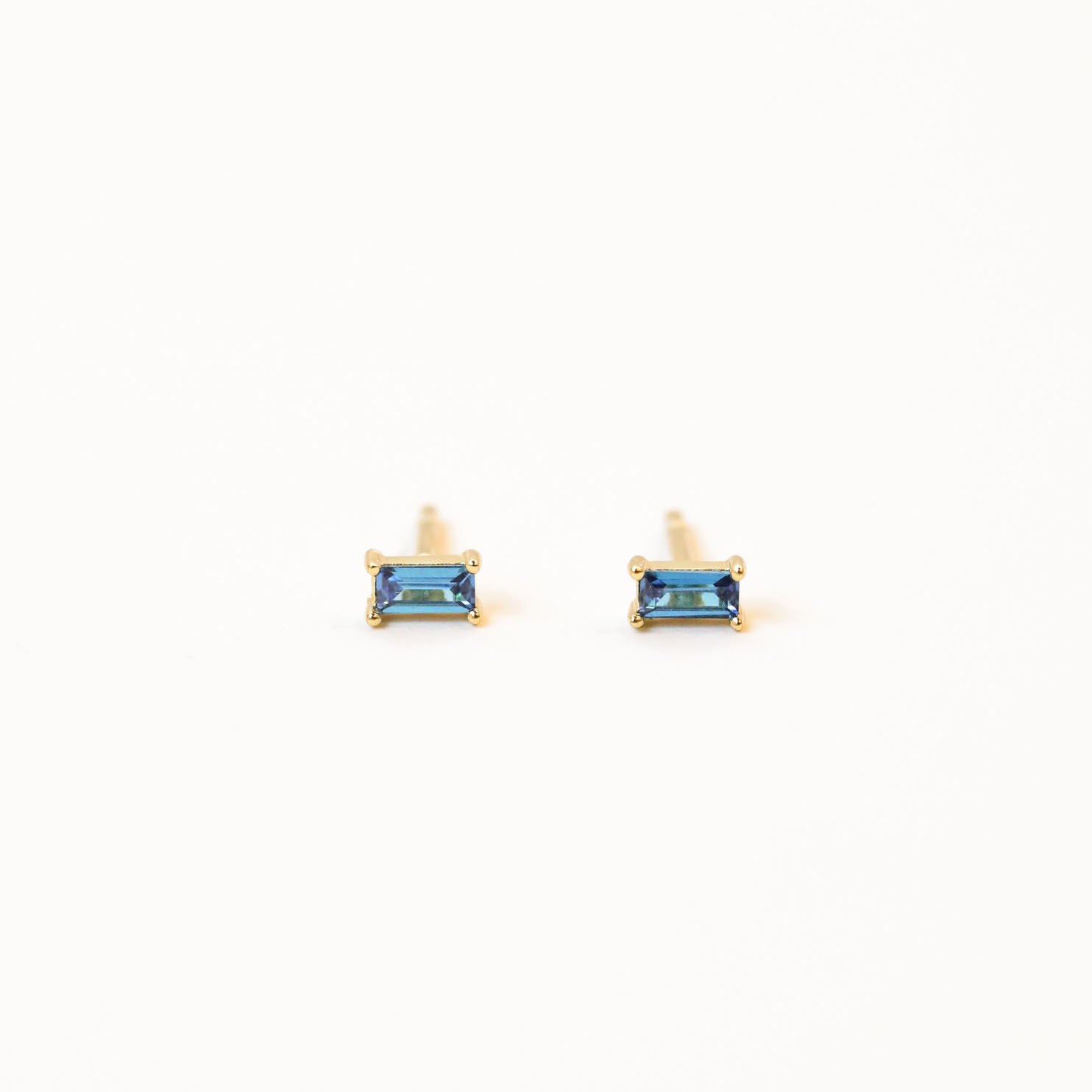 Sapphire Baguette: small, rectangular blue stud earrings set in gold, shown against a plain white background.
