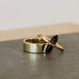 Two gold rings rest on a dark surface: a classic band and the Smoky Quartz Point Ring, featuring a double-pointed smoky quartz crystal set horizontally—ideal for fans of minimalist jewelry.