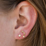 A close-up of a person’s ear featuring three 18k gold plated Star & Constellation earrings arranged in a curved line up the earlobe, with light brown hair beside the ear accentuating this celestial charm.